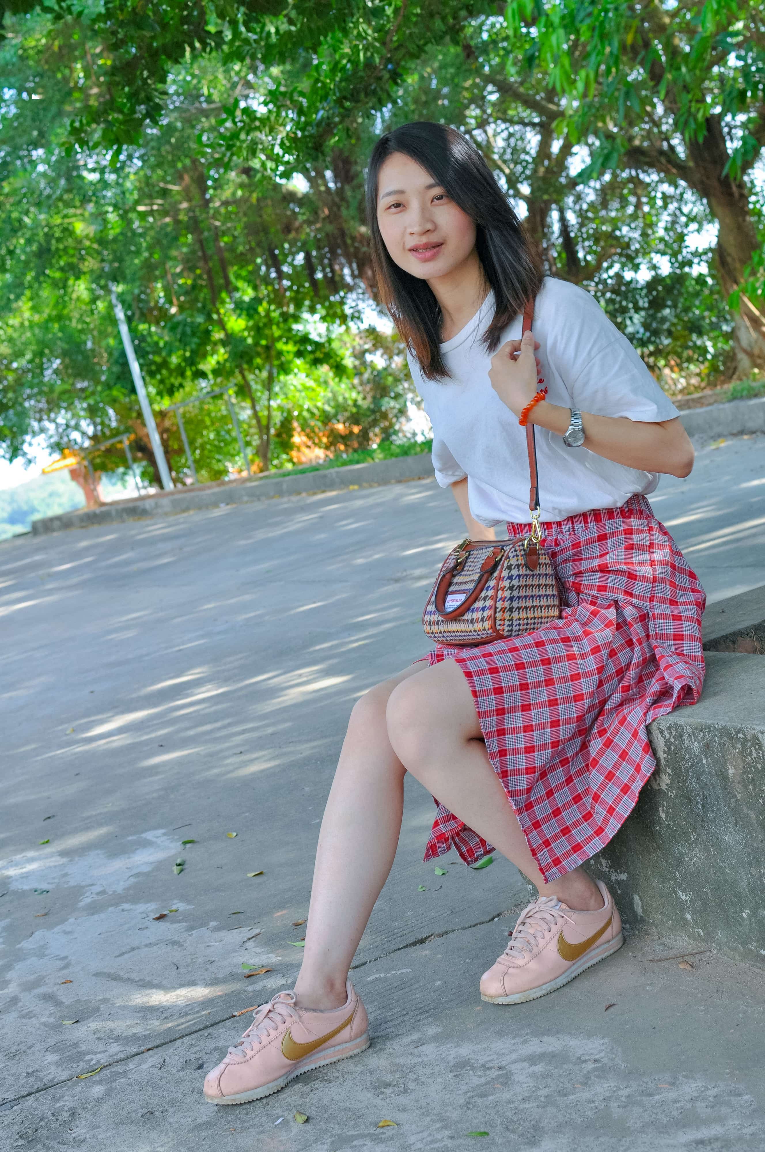 Young woman in plaid skirt removing nylon, bare sole revealed, sneakers by her side