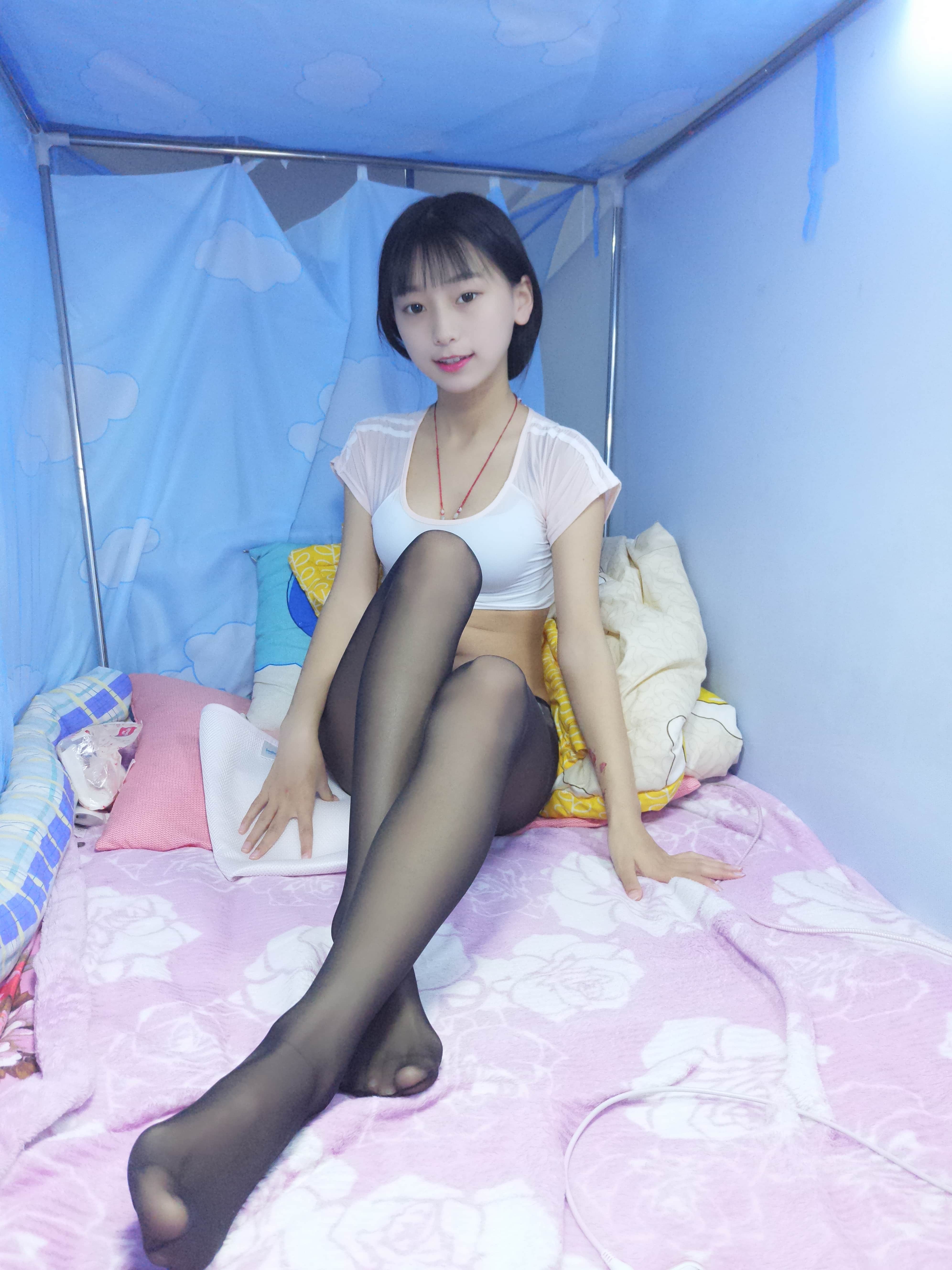 Moody shot of legs in black nylon, feet crossed with shine highlighting calf curves against rumpled sheets.