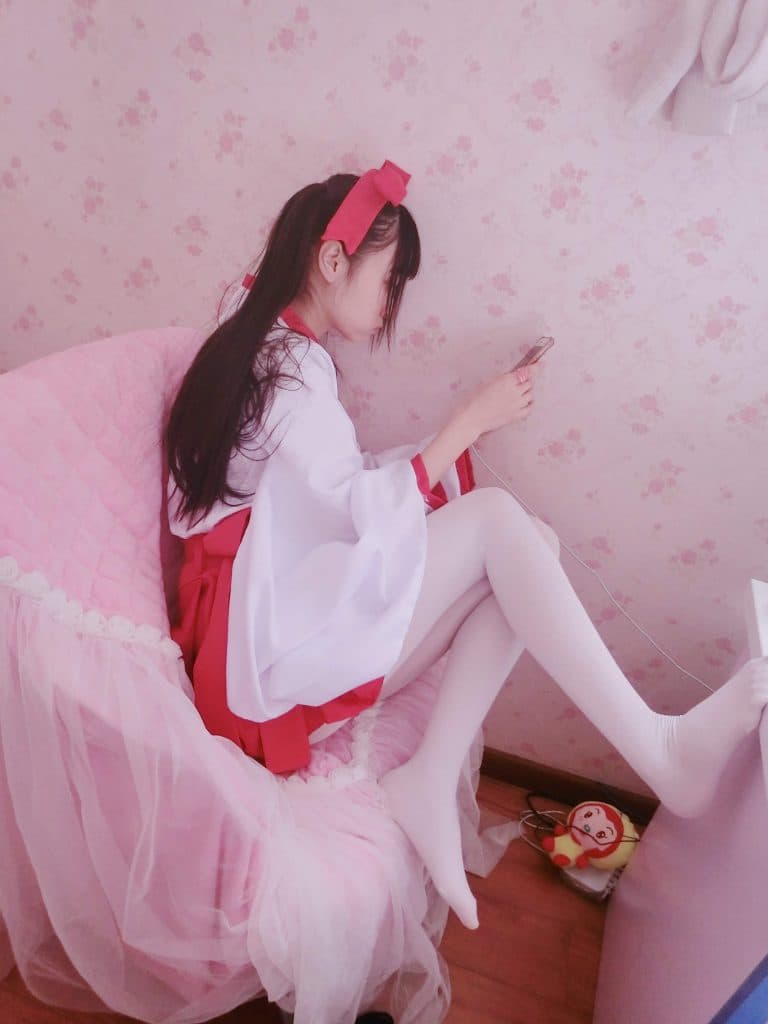 Adult shrine-maiden cosplay with flowing robes, stockings peeking out, and a bare foot gently touching a woven mat