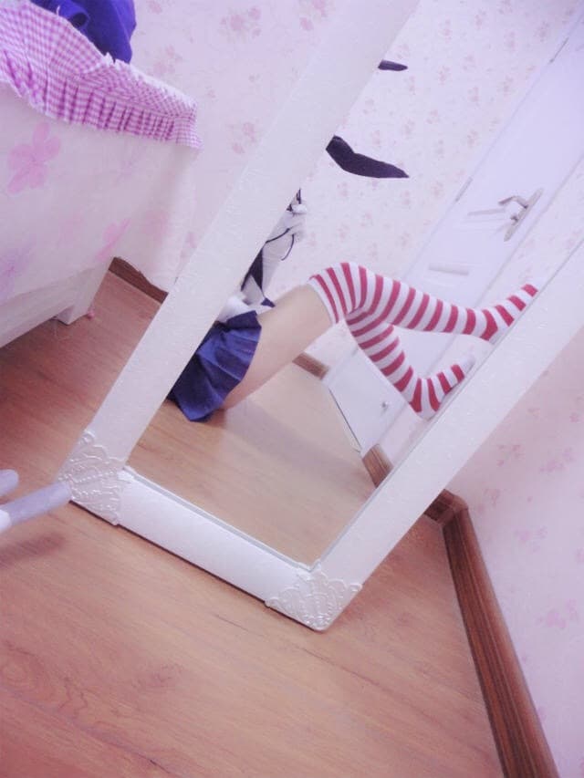 Playful cosplay shot showing nylon-clad legs, nautical accessories, and a bare foot resting on a striped cushion