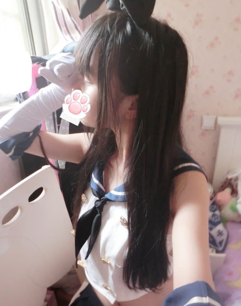 Cosplay-inspired pose with glossy stockings, naval ribbons, and bare feet peeking from beneath a short skirt