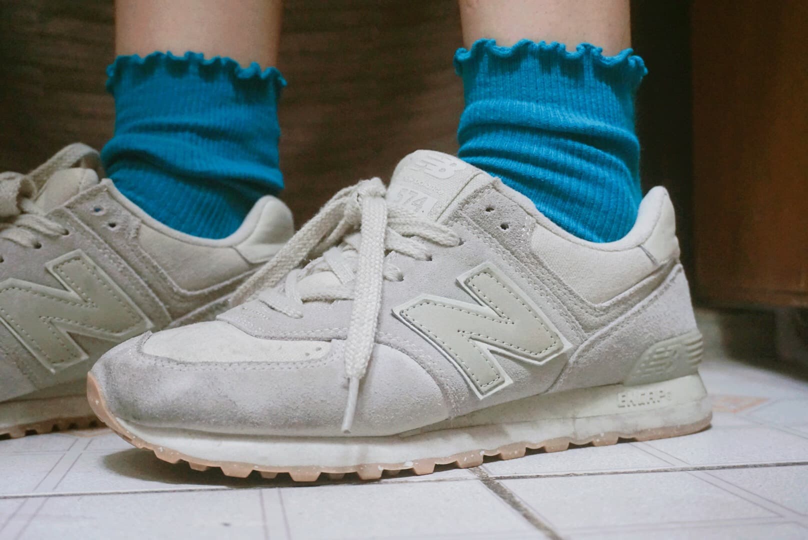 Casual close-up of feet in faded blue cotton socks slipping into scuffed n-brand sneakers, soft fabric texture visible.