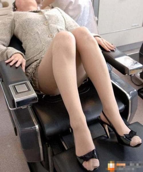 Woman seated on salon chair wearing sheer stockings, legs crossed, polished nails and a glossy nylon sheen catching studio lights