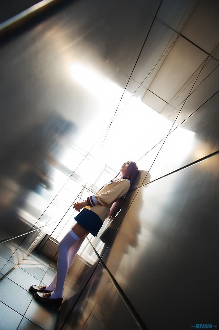 Adult model wearing a school-style uniform sits with legs extended, showcasing thigh-high socks and arched feet in studio lighting