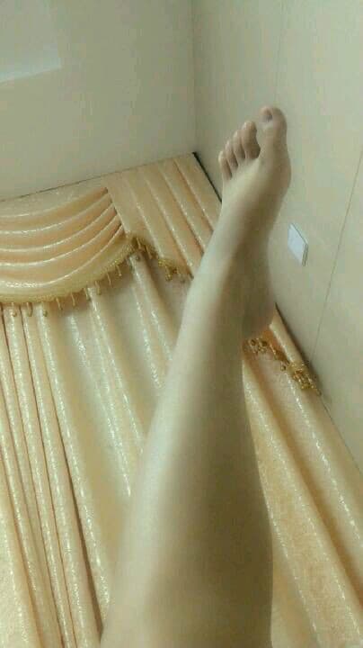 Softly lit close-up of petite adult feet with neat nails, toes gently curled on a plush pillow creating an intimate mood