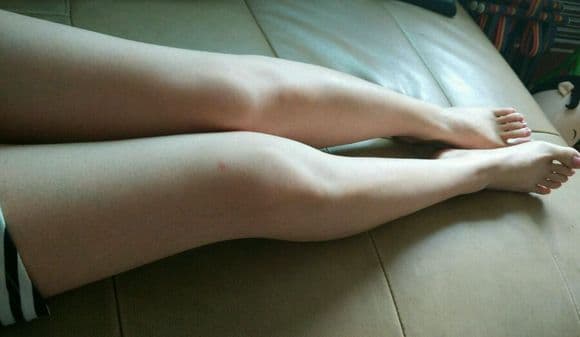 Close-up of bare adult feet resting on satin sheets, toes slightly curled with soft side lighting enhancing skin texture