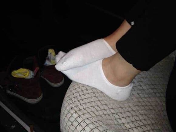 Wife seated on couch pulling on white boat socks, bare ankles and soft fabric folds visible
