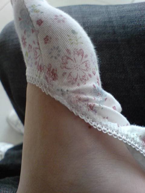 A guest sits on a doorstep removing boat socks, fingers easing fabric down past the heel, warm tones.