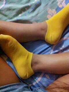 Bright yellow socks, slightly rumpled, lying beside a barefoot with heel just exposed.