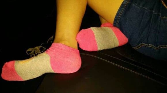 Pair of feet in soft pink cotton socks curled on a sofa, toes pressing lightly against the fabric.