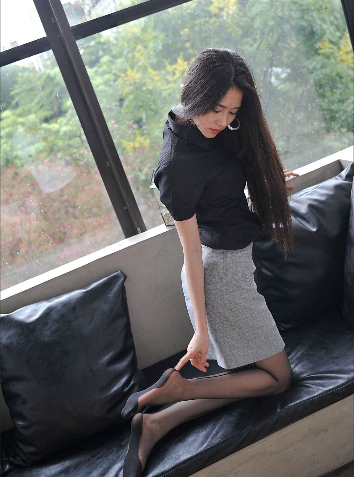 Woman in tailored uniform sitting with crossed legs, sheer stockings shimmering, knees close together in a suggestive, grown-up tableau.