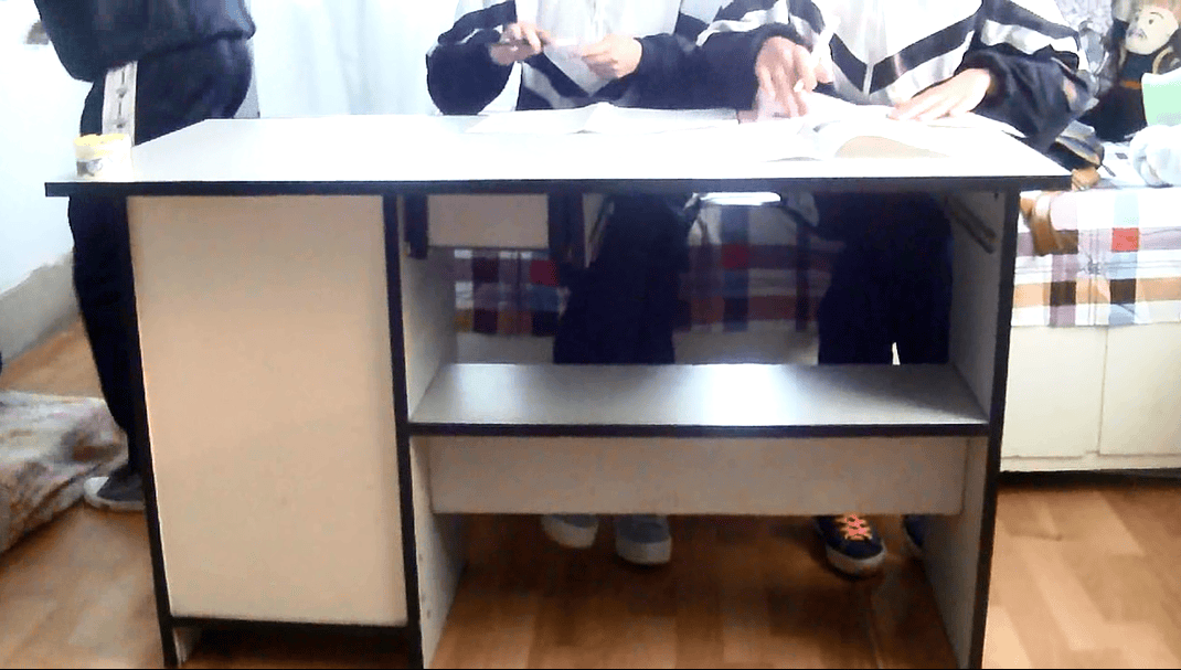 Three adult women seated at a table, legs and bare feet visible, stockings rolled down, intimate study scene in warm light.