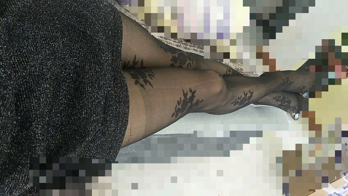 Confident male figure seated, stockings rolled to ankle revealing smooth calf and toes in sheer nylon light