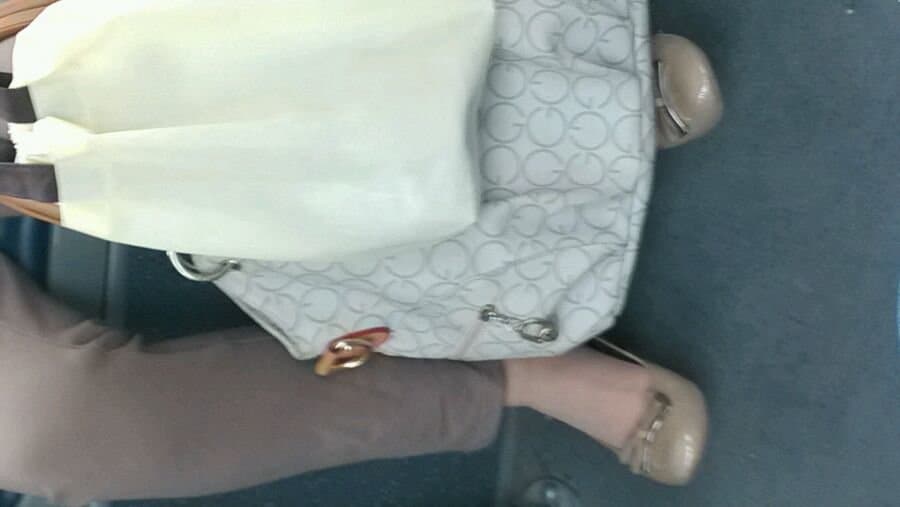 Candid bus photograph showing stockinged ankle tucked under seat, lace trim visible amid public commute surroundings.