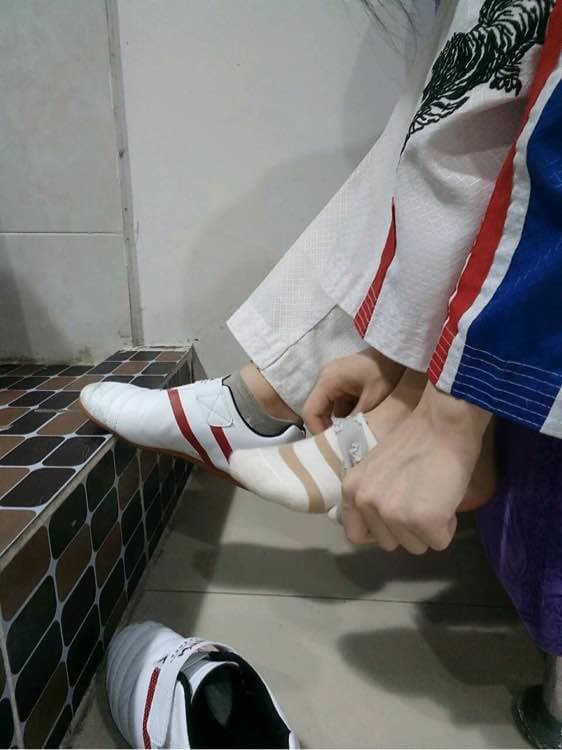 Athletic adult in taekwondo outfit lounges after training, stocking-clad legs and one bare foot flexing in a relaxed, sensual pose.