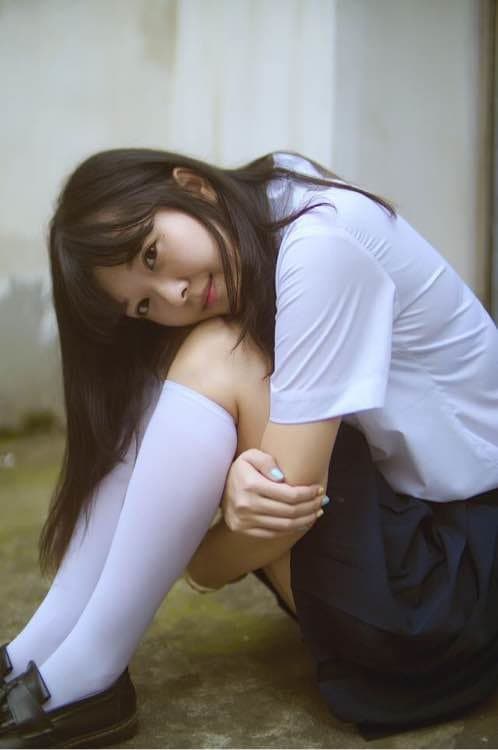 Shy adult newbie sits on a bed, peeling down sheer stockings to reveal a white cotton sock and delicate bare toes beneath.