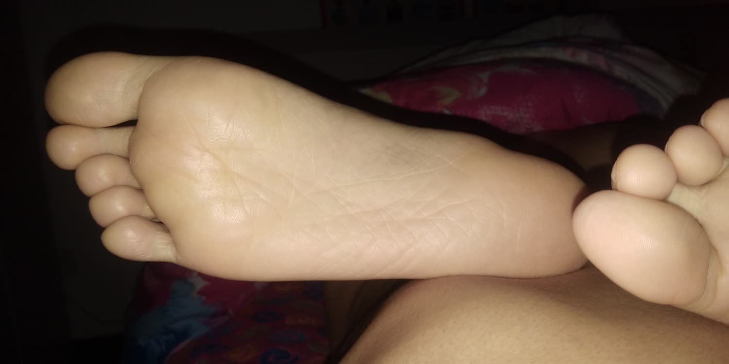 Tender hands holding a girlfriend's bare foot, stockings nearby and a soft, affectionate atmosphere with warm indoor lighting