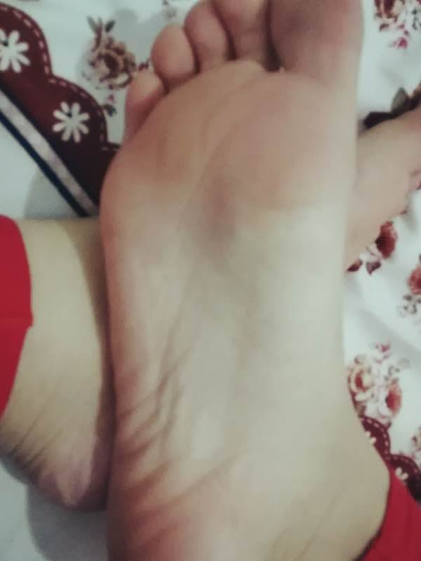 Close-up of a wife's bare feet resting on satin sheets, toes slightly curled in soft evening light