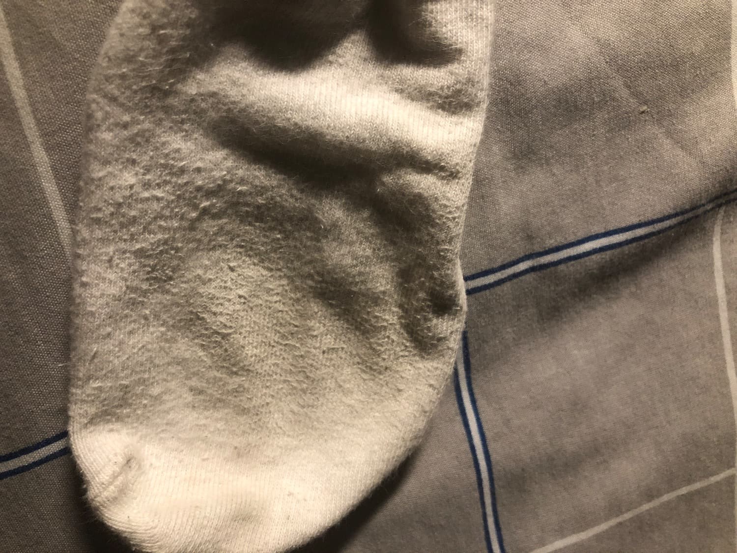 Feet silhouette beneath thin socks, toes faintly pressing into soft fabric on a bed