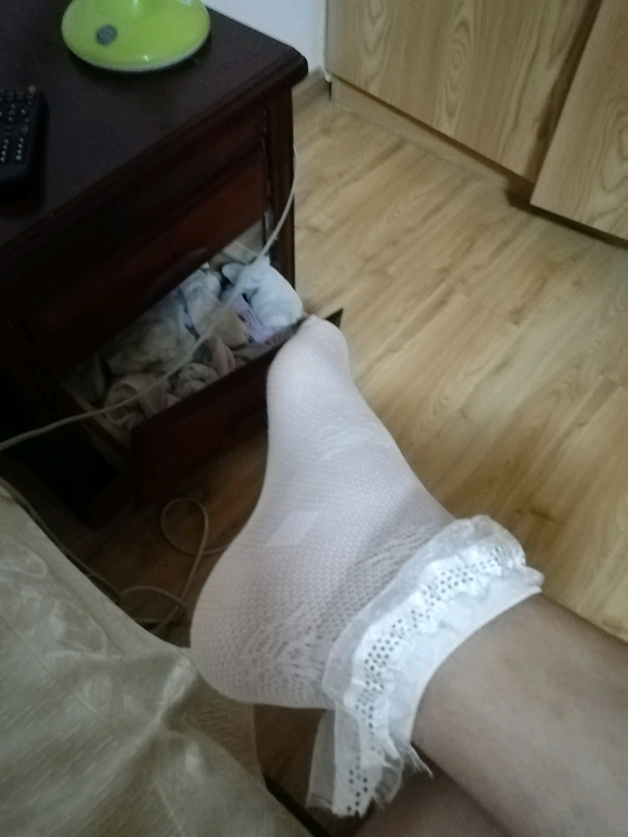 Soft white ankle socks slightly rumpled on feet, fabric hugging toes and heels with familiar creases and delicate texture.