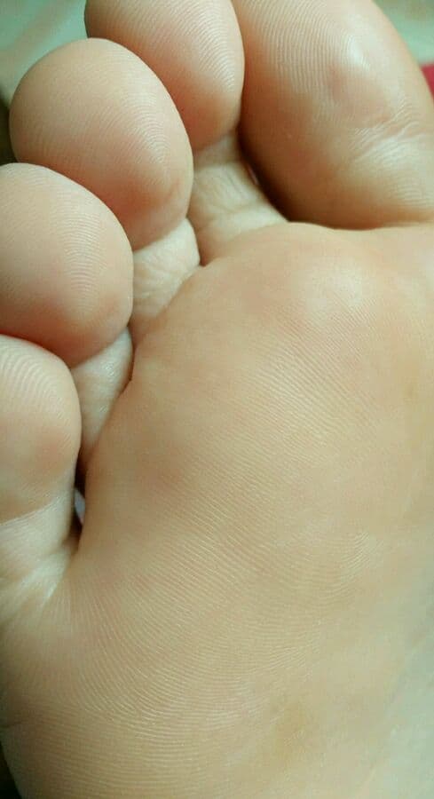 Tender close-up of girlfriend’s bare foot with soft arch visible, toes relaxed and skin luminous