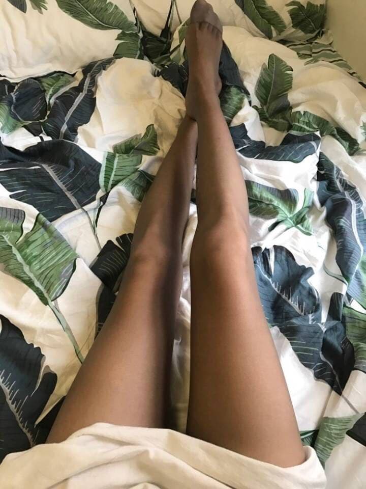 Bare feet resting on pristine bed sheets with a stray silk stocking nearby