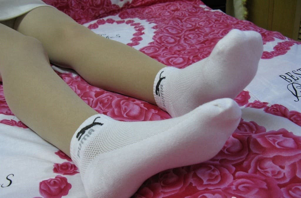 White cotton socks rolled at the ankle next to sheer stockings, playful contrast on a warm wooden floor