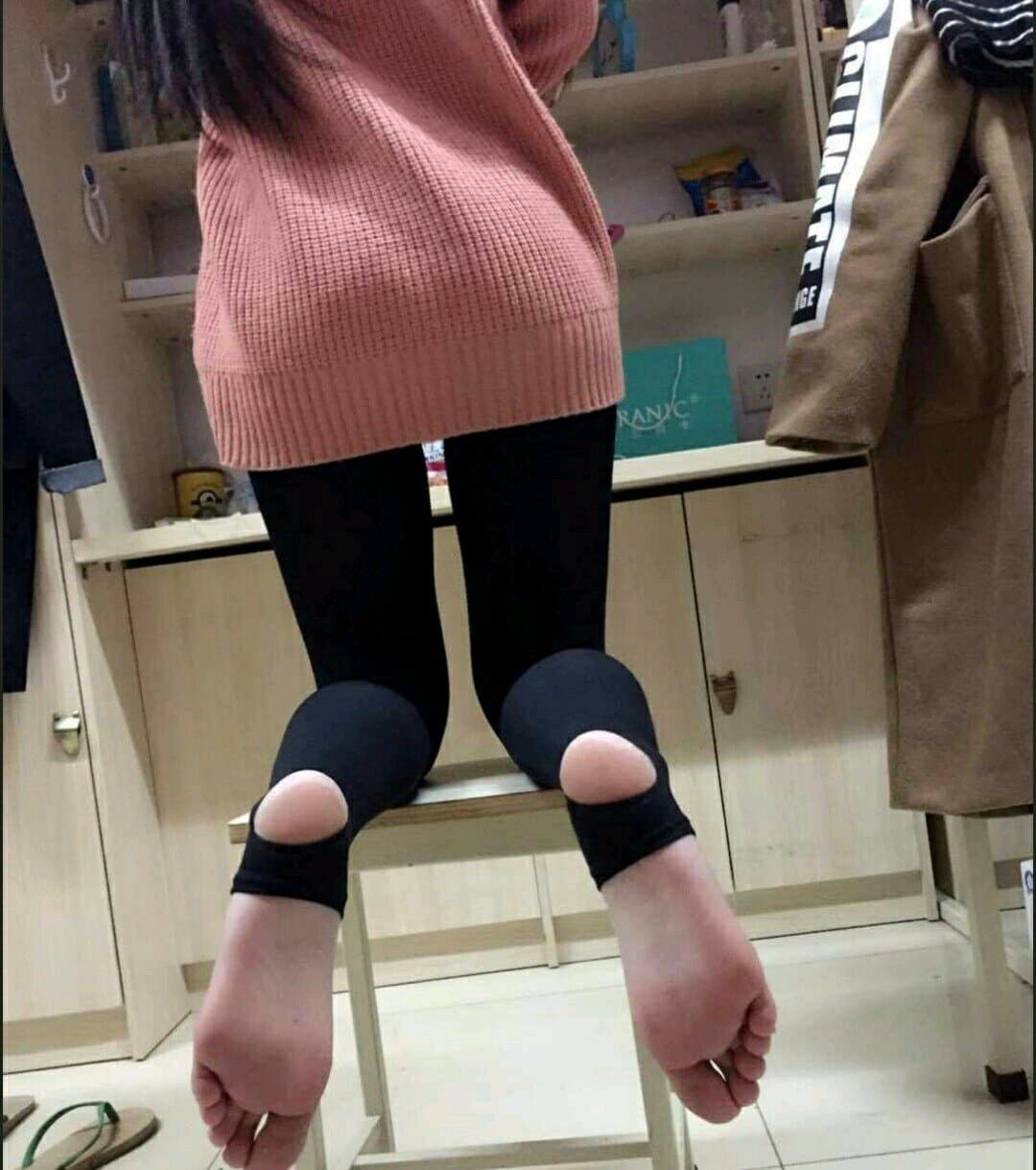 Two adults on a sofa, one playfully asking for help while bare toes brush against worn cotton socks