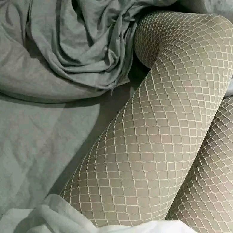 Pair of feet alternating between bare and nylon-clad, toes softly pointed and stocking sheen catching the light.