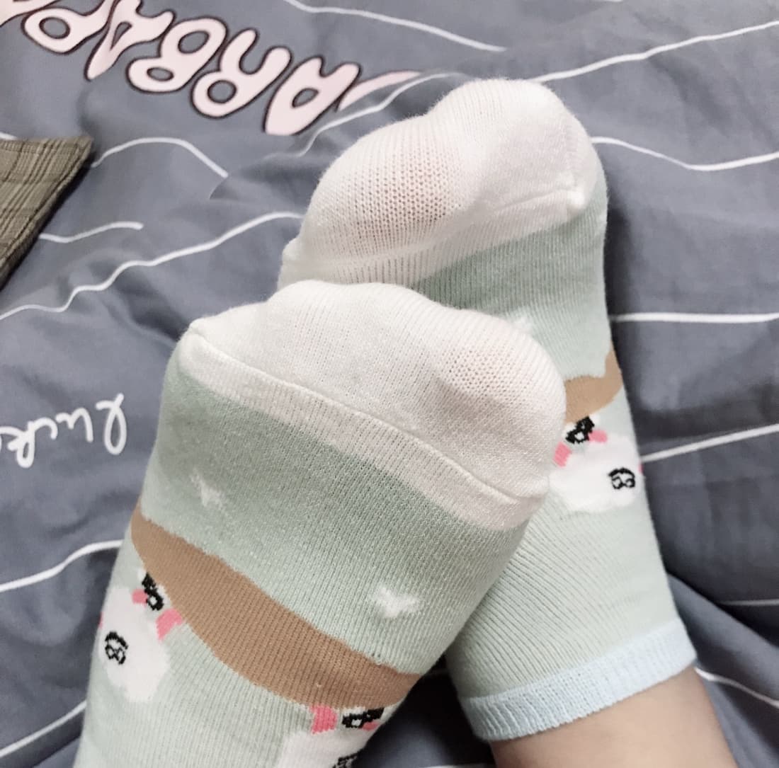 Close-up of bare Asian feet on soft sheets, sheer stockings slipping down over delicate arches