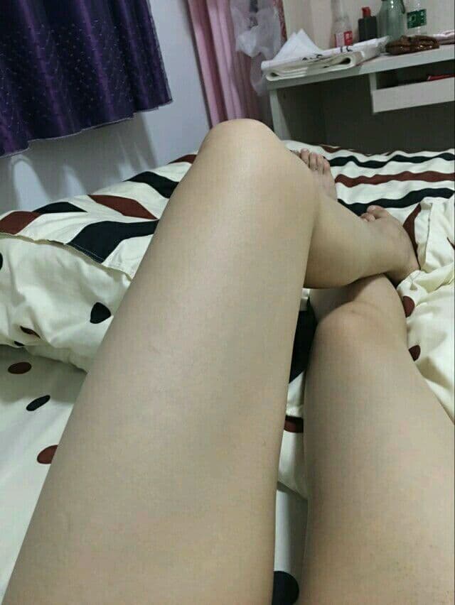 Close-up of bare feet arched on soft bedding with sheer nylon glinting under warm lamplight.