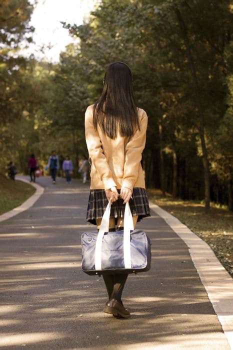 Adult woman sunlit on wooden floor showing bare soles, sheer stockings rolled at ankles, autumn leaves scattered around her.
