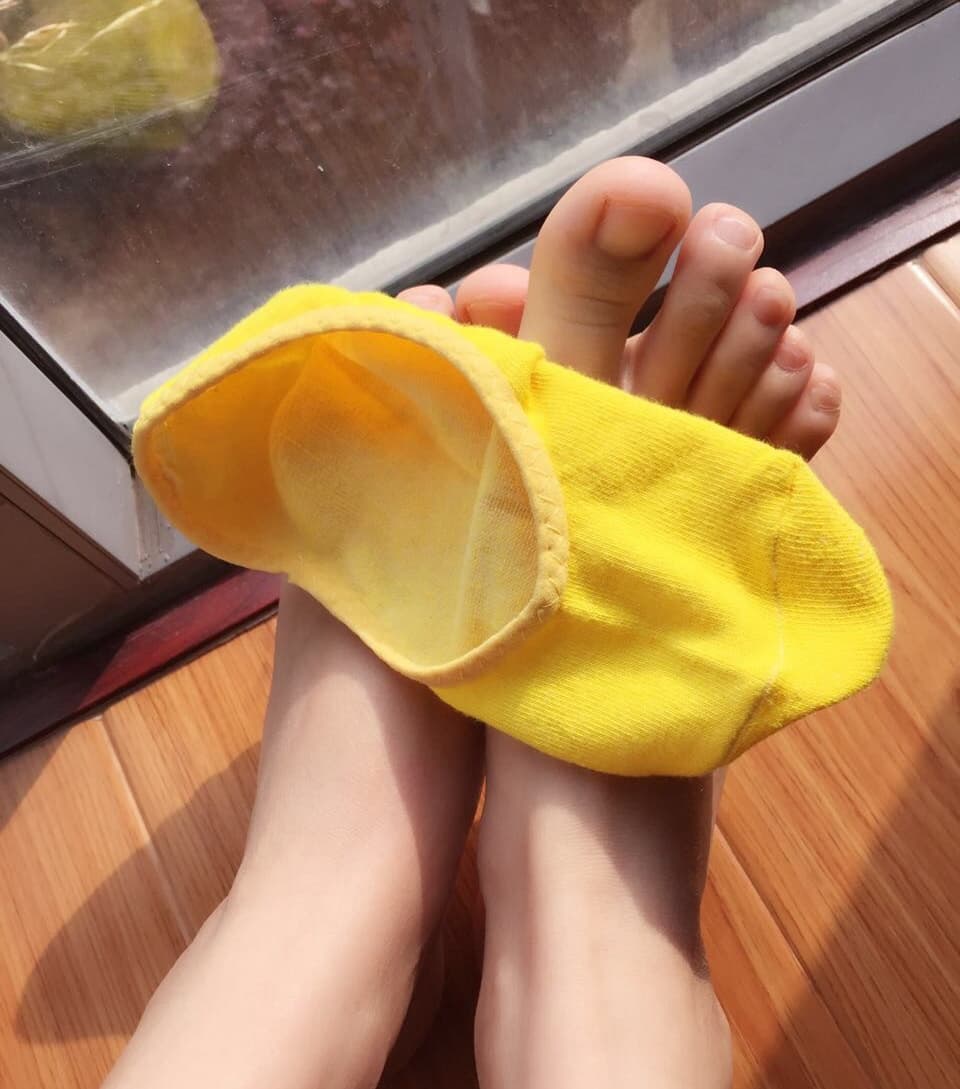 Pair of feet wearing mismatched white and yellow socks, one foot half exposed with playful toe peep