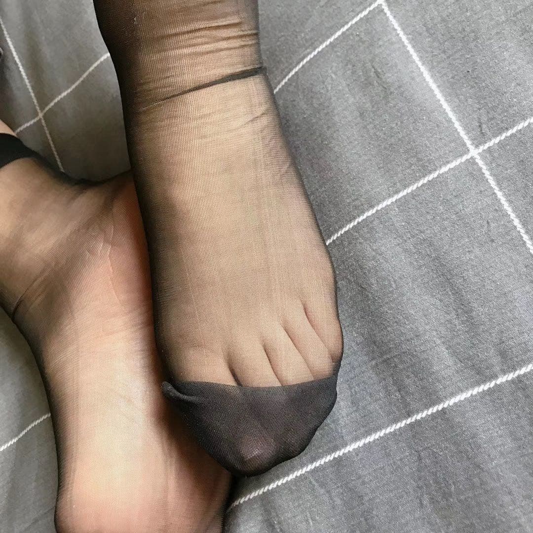 Preview close-up of nylon-clad toes and exposed sole, glossy fabric catching warm ambient light in intimate framing.