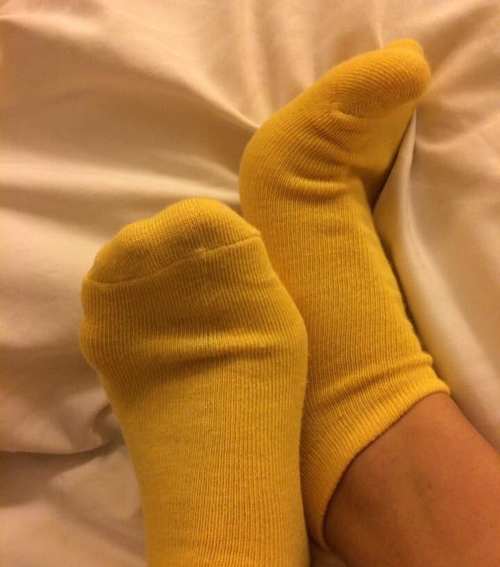 Yellow home socks loosely covering petite feet as toes peek out, hinting at cozy, lived-in comfort and intimacy.