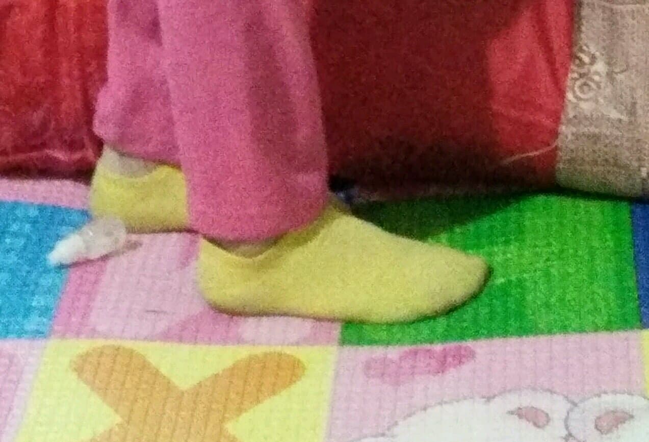 Playful adult companion teasing with a sock half-removed, bare ankle exposed, toes wiggling slightly in a cozy indoor setting.