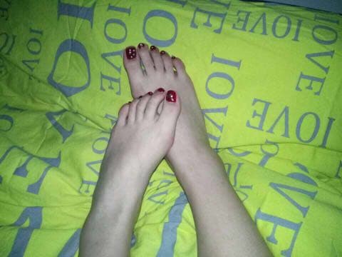 Softly lit close-up of bare feet with arched instep and delicate toes on satin sheets