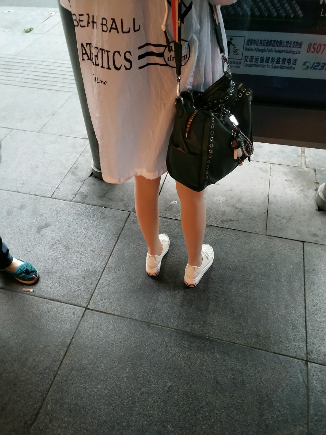 Nighttime street shot of multiple legs in sheer pantyhose, city lights reflecting off nylon and polished heels on pavement.