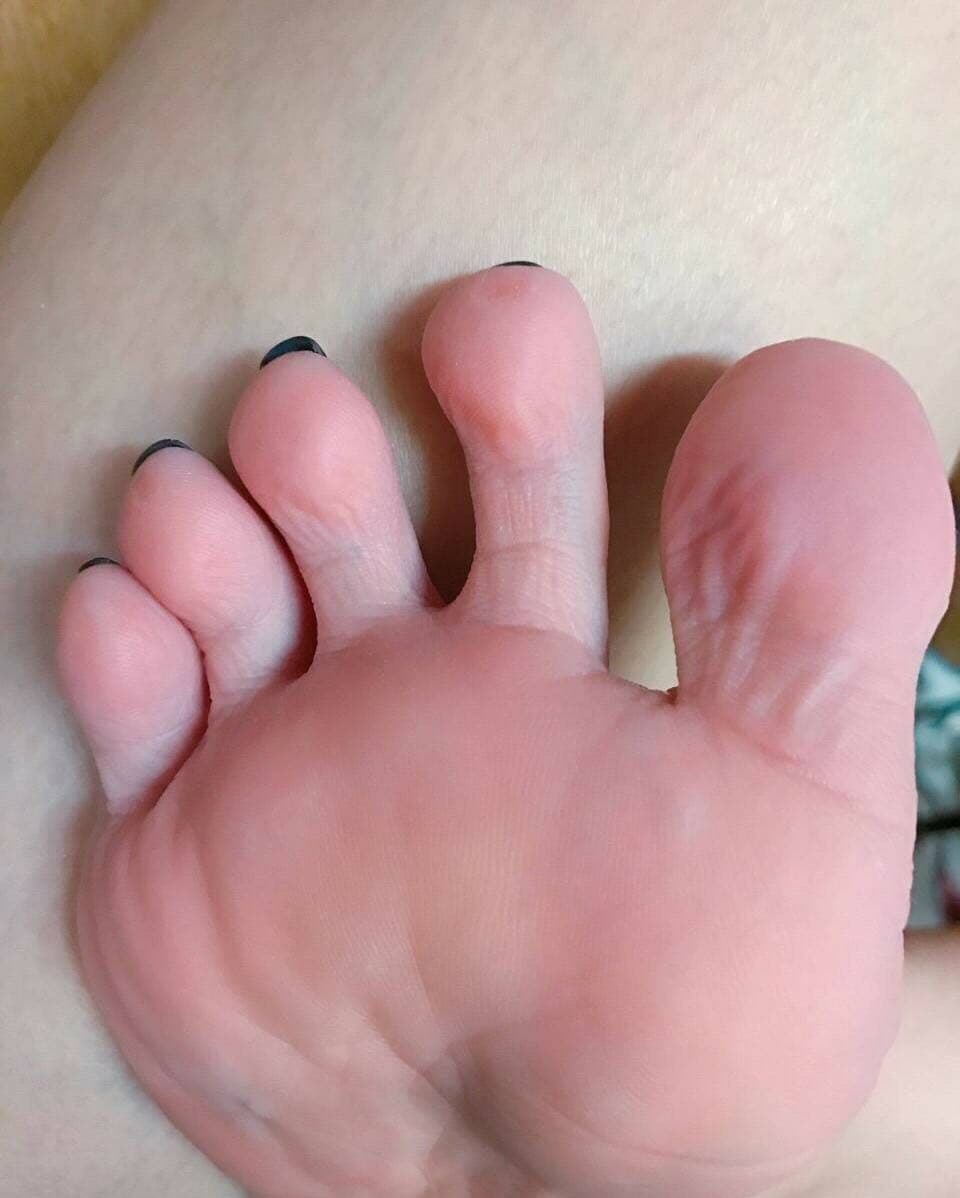 Close-up of silk stockings sliding down a sunlit ankle, toes curling slightly, shimmering nylon against smooth skin in soft light.