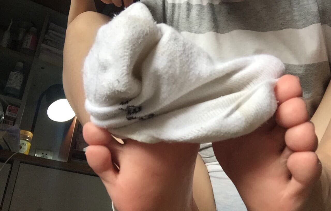 Pairs of cotton socks discarded at ankles, slightly rumpled and stained, exposing bare soles with warm skin tones