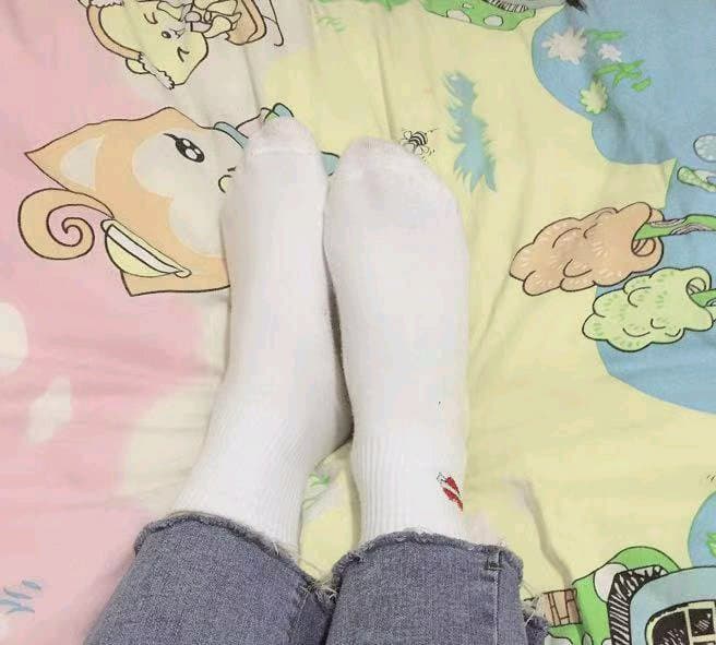 Pair of white cotton socks loosely scrunched around ankles on a hardwood floor, toes peeking and soft sunlight nearby.