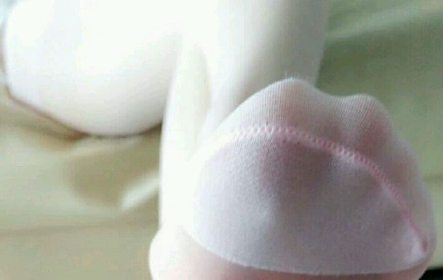 Close-up of a satin-clad foot arch with nylon sheen and delicate toes curled against soft fabric.