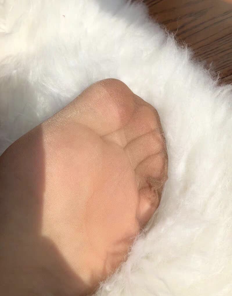 Angled view of bare soles resting on a plush blanket with nylon stockings rolled around the ankles