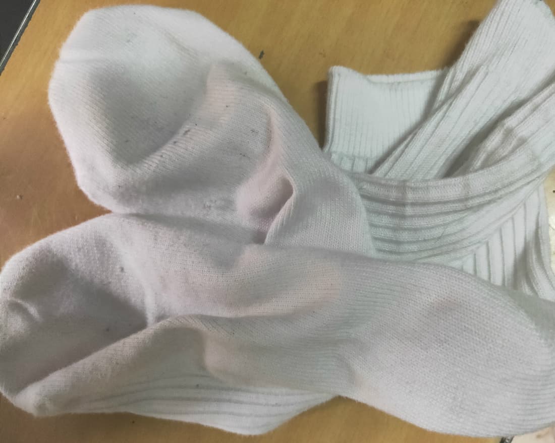 Pair of cotton uniform socks folded at the ankle with soft creases and warm tones