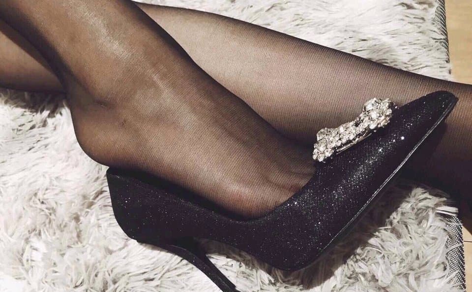 High-heeled foot resting on a silk cushion, stocking seam taut, exuding confident dominance and inviting admiration.