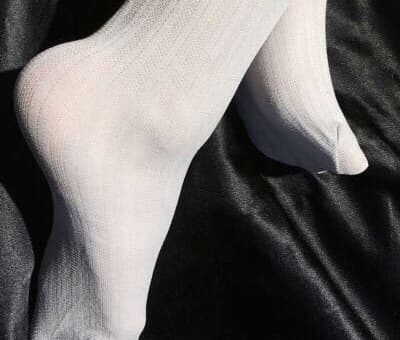 A pair of glossy black thigh-high stockings clinging to long legs, seam tracing down the calf toward a lacy top.