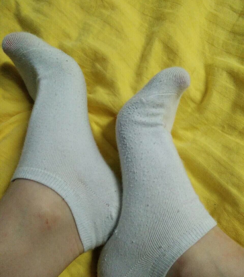 Close-up of bare feet in crumpled white cotton socks, toes slightly curled, soft heel creases visible against warm skin.