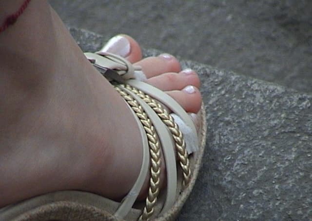 Street-level close-up of beautiful feet stepping on pavement, sheer stockings and bare heel visible, urban textures contrasting