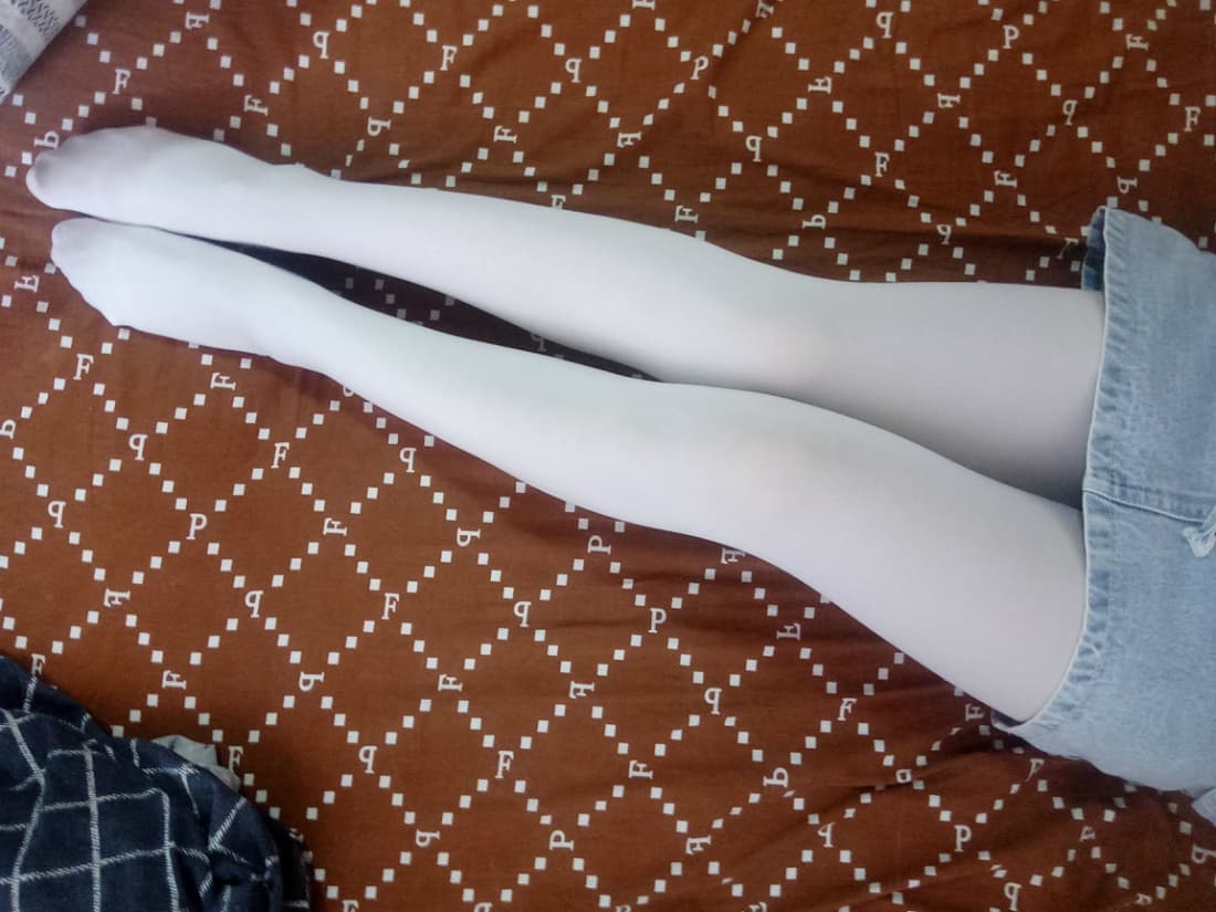 Close-up of bare Asian feet slipping out of sheer nylon stockings, toes curled against soft fabric, intimate studio lighting