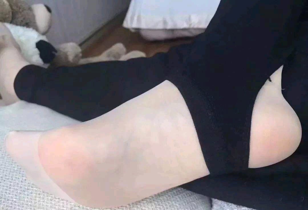 Side view of bare foot peeking from beneath a nylon stocking, ankle curved and toes softly flexed in a relaxed pose.